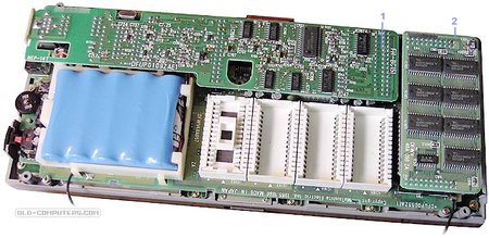 "The upper side of the logic board holds the battery, the four ROM sockets as well as two piggi-back cards, the Serial interface card (1) and the 128 KB RAM card (2)."
